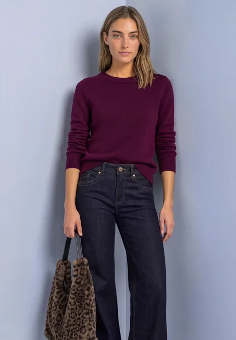Femme en pull violet foncé, jean ample et sac léopard, posant devant un fond clair.