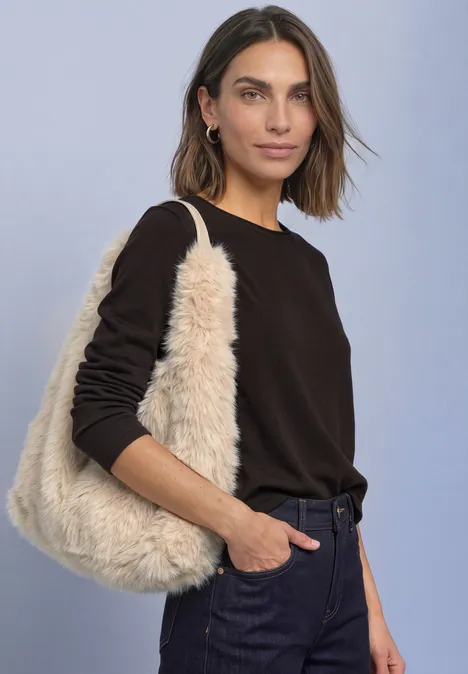 Frau in schwarzem Pullover präsentiert eine cremefarbene, flauschige Teddy-Tasche vor hellem Hintergrund.