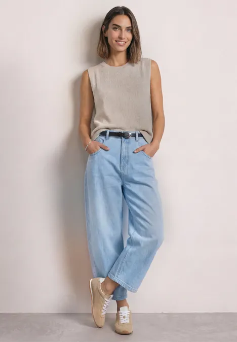 Smalle riem met decoratieve gesp Black Frau in beigem Top, hellblauen weiten Jeans und beigen Sneakern vor hellem Hintergrund.