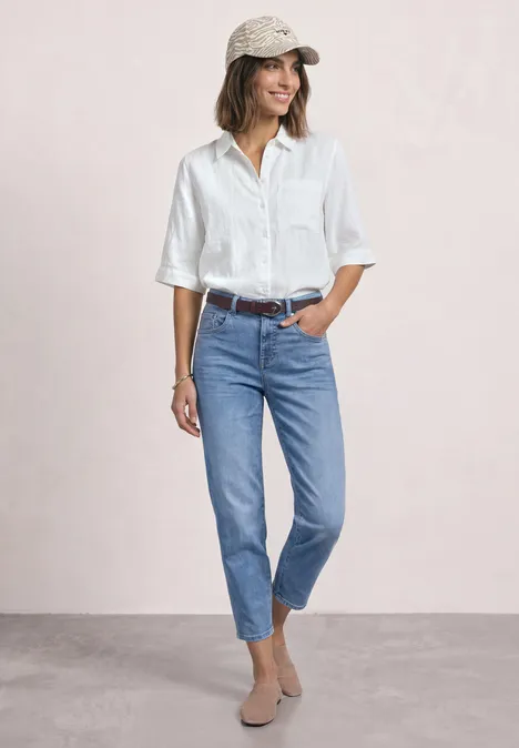 Smalle riem met decoratieve gesp rustic rouge Frau in weißer Bluse, blauen Jeans, beigen Boots und Basecap steht entspannt vor hellem Hintergrund.