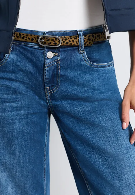 Vrouw draagt blauwe jeans met luipaardriem en wit topje
