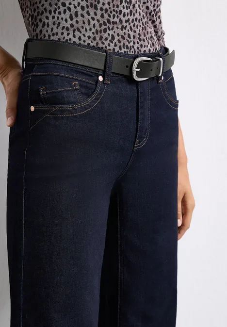 Dunkelblaue Jeans mit schmaler Passform, kombiniert mit einem schwarzen Gürtel vor weißem Hintergrund.