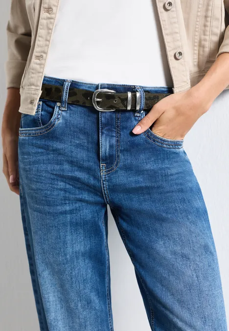 Person trägt blaue Jeans mit schwarzem Gürtel und weißem T-Shirt unter heller Jacke.