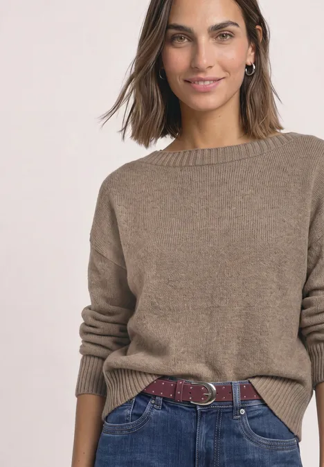Velours Gürtel mit Nieten rustic rouge Frau in braunem Strickpullover, blauen Jeans und rotem Flechtgürtel, lächelnd.