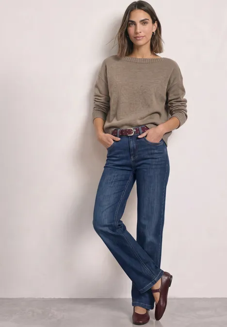 Velours Gürtel mit Nieten rustic rouge Eine Frau mit braunem Pullover, blauen Jeans und braunen Slippern lehnt entspannt an einer Wand.