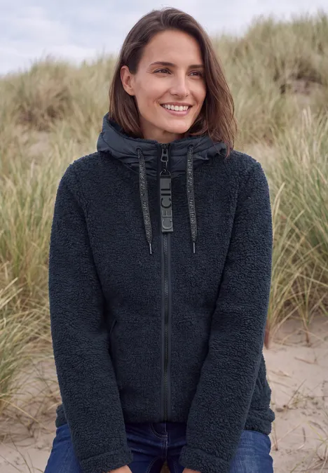 Lächelnde Frau im dunklen Fleece-Hoodie vor Strandgras