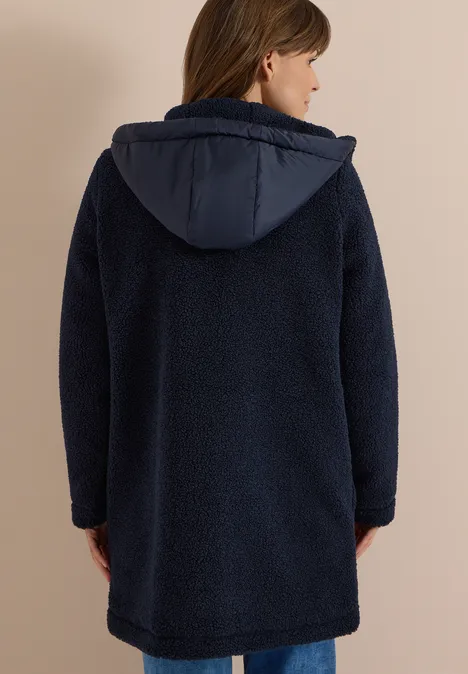 Frau von hinten in einem dunkelblauen, knielangen Teddy-Fleece-Mantel mit Kapuze.