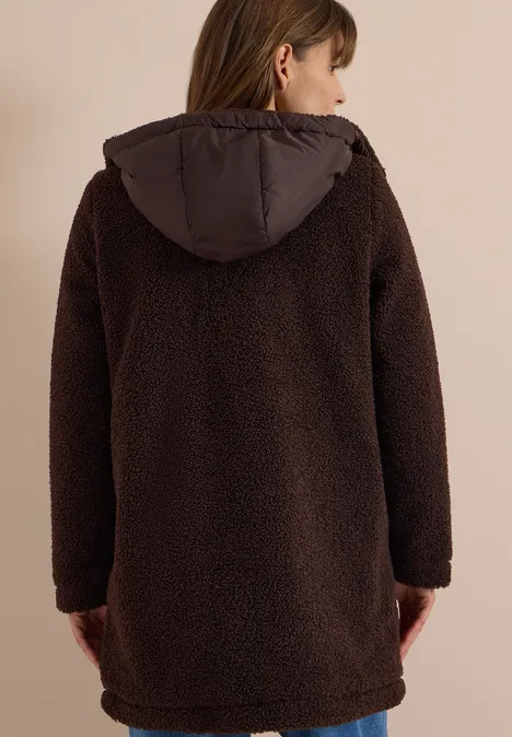 Rückansicht einer Person in einem braunen, langen Teddyplüsch-Mantel mit Kapuze.