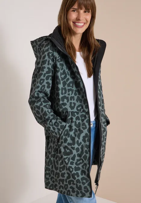 Softshell-jas met capuchon en luipaardprint shadow khaki Frau lächelt in einem grünen Mantel mit Kapuze und schwarzem Leopardenmuster.