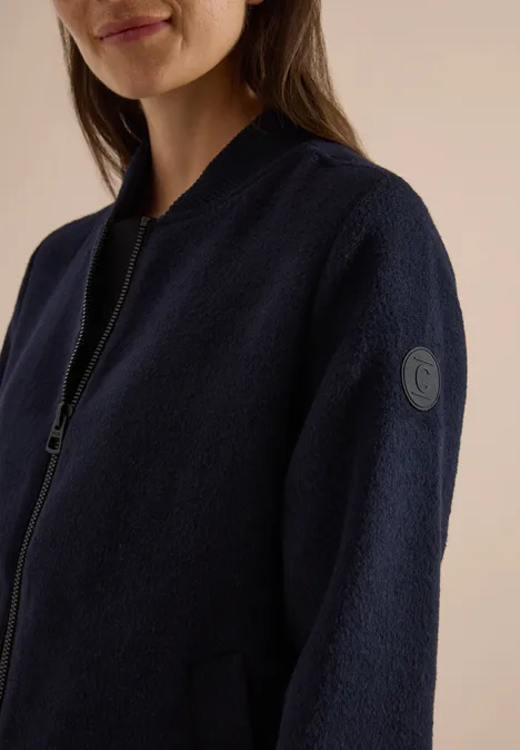 Frau in dunkelblauer Fleece-Jacke mit Reißverschluss und rundem Logo am Ärmel