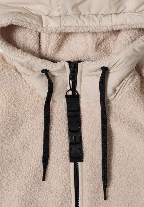 Close-up van een beige teddyfleece-jas met zwarte rits en koorden