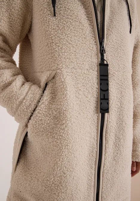 Close-up van een beige teddyfleecejas met ritssluiting en zijkanten zakken.