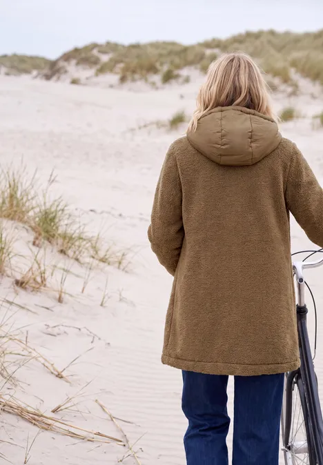 Personne en manteau brun pousse un vélo sur les dunes de sable d'une plage.