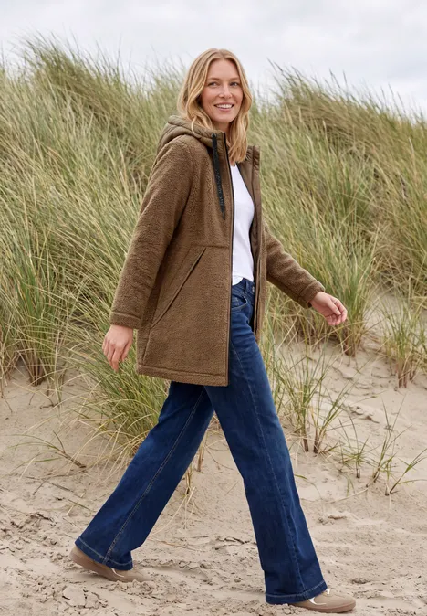 Une femme se promène joyeusement sur la plage devant des dunes de sable.