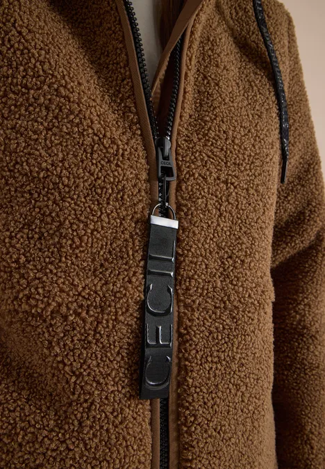 Close-up van een bruine fleecejas met rits en leren ritshanger.