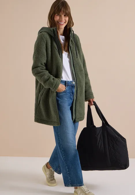 Vrouw in groen teddyjack, spijkerbroek en sneakers, met grote zwarte tas