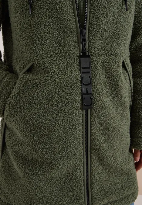 Close-up van een groene teddyfleecejas met rits en zakken.