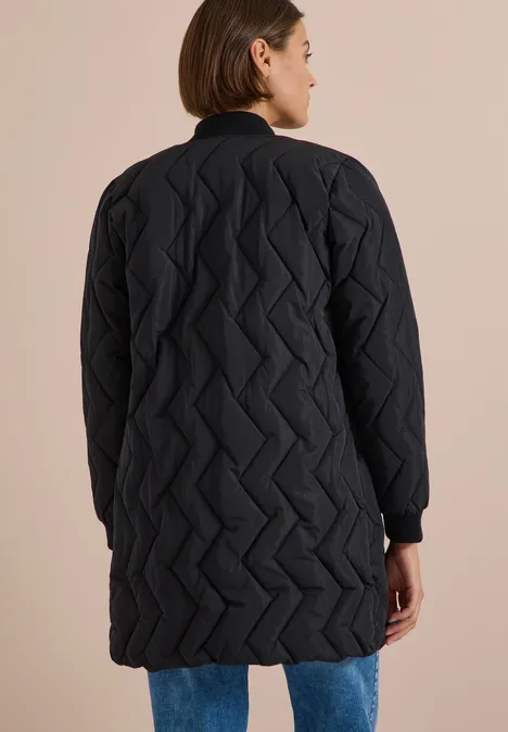 Femme de dos portant un manteau matelassé long noir à motif zigzag.