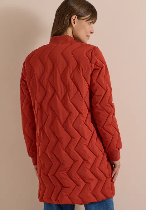 Langer Blousonmantel mit Steppmuster light russet red Rückansicht einer Frau in einem roten, gesteppten, knielangen Mantel vor neutralem Hintergrund.
