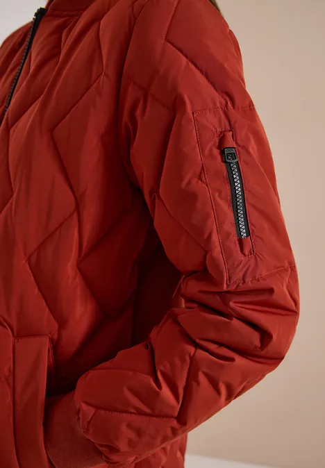 Langer Blousonmantel mit Steppmuster light russet red Rote, gesteppte Winterjacke mit Reißverschlusstasche am Ärmel vor neutralem Hintergrund.
