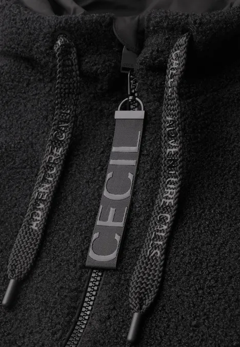Gros plan d'une veste polaire noire avec fermeture éclair, cordons et une breloque portant 'CECIL'.