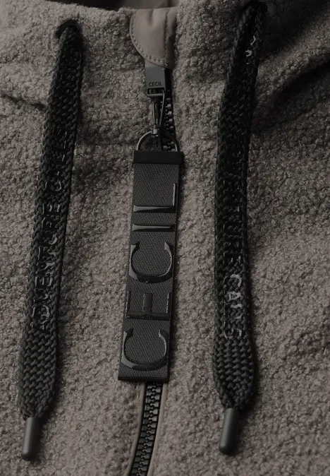 Nahaufnahme eines Reißverschlusses mit CECH-Logo und Kordeln an einem Fleece-Hoodie.