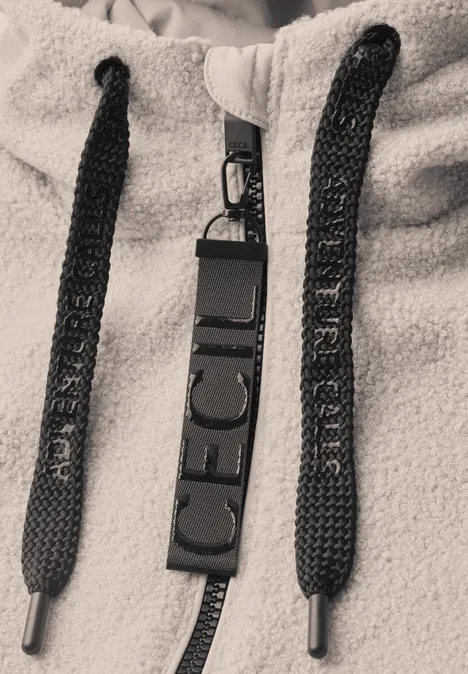 Nahaufnahme eines beigen Fleece-Hoodies mit schwarzen Kordeln und einem schwarzen Tag mit Aufschrift ICE CUBE.