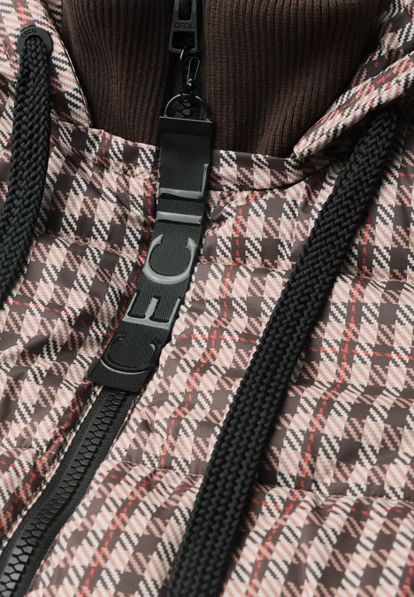 Close-up van een jas met bruin-beige pied-de-poule motief, zwarte ritssluiting en zwarte koorden