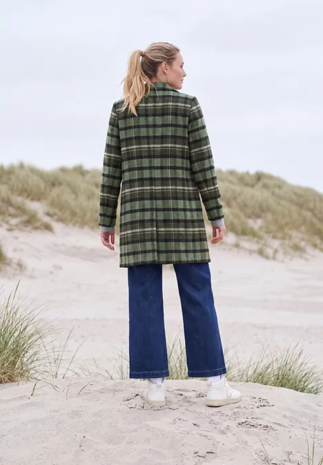 Reversmantel in Wolloptik shadow khaki Frau von hinten in grün kariertem Mantel, blonder Pferdeschwanz, Jeans und weißen Sneakern auf Dünen.
