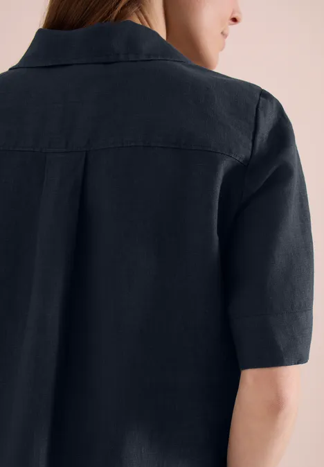 Rückansicht einer Person mit halblangem braunem Haar in schwarzem Leinenhemd mit Kurzarm.