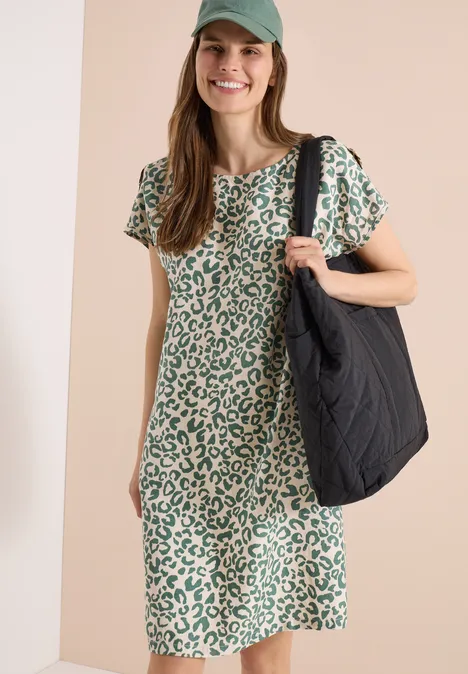 Frau in grünem Leopardenmuster-Kleid trägt große schwarze Tasche.