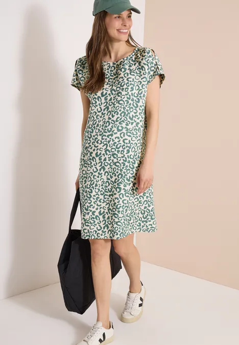 Frau trägt grün-weiß geblümtes kurzärmliges Midi-Kleid, weiße Sneakers und schwarzen Shopper.