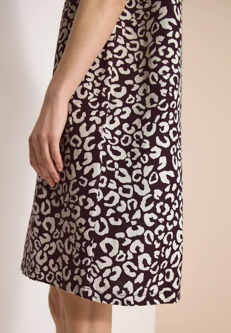 Seitliche Ansicht eines knielangen Kleides mit weißem Animal-Print auf dunklem Untergrund und sichtbarer Hand.