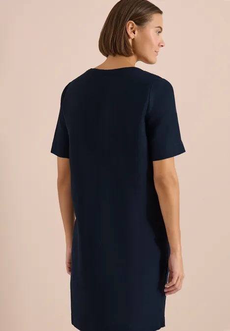 Frau von hinten in einem schlichten, kurzärmligen, dunkelblauen Kleid