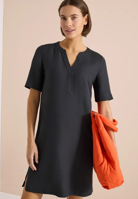 Dunkelblaues, knielanges Kleid mit V-Ausschnitt, kurzen Ärmeln, Frau hält orange Jacke.