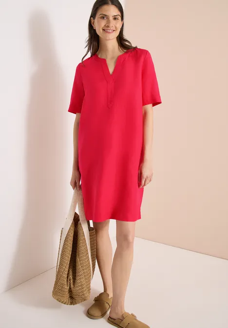 Frau in lockerem roten Kleid, beige Sandalen und hält eine geflochtene Strohtasche.