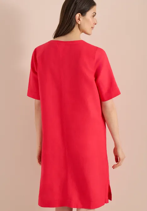 Eine Frau trägt ein schlichtes rotes Kleid, Rückenansicht.