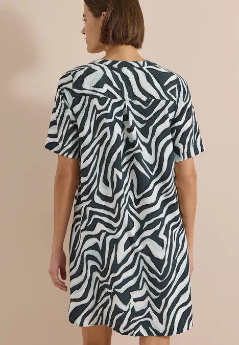 Frau in kurzem, zebra-gestreiftem Kleid, Rückenansicht vor neutralem Hintergrund.