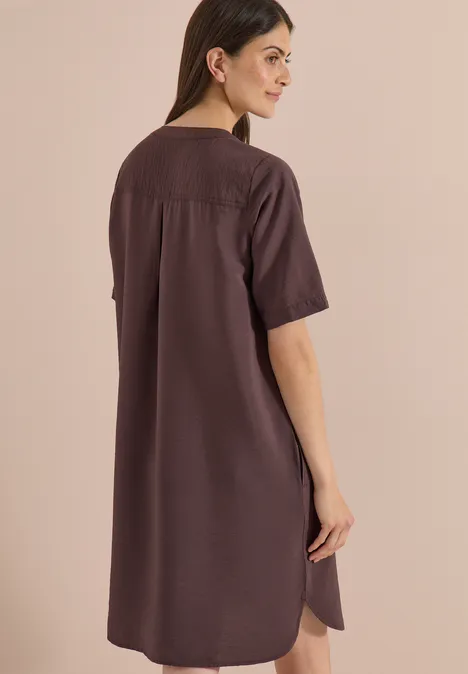 Knie-lange jurk met split in de hals brown cacao Rugaanzicht van een vrouw in een losse, donkerbruine, knie-lange jurk met korte mouwen.