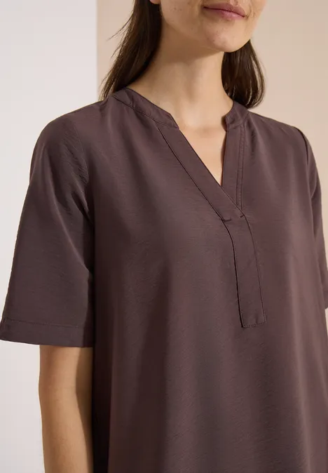 Knie-lange jurk met split in de hals brown cacao Vrouw draagt een simpele, korte mouw, bruine blouse met V-hals en rechte pasvorm tegen een lichte achtergrond.