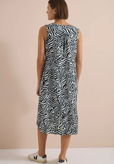 Eine Frau trägt ein ärmelloses, knielanges Kleid mit schwarz-weißem Zebra-Muster vor neutralem Hintergrund.