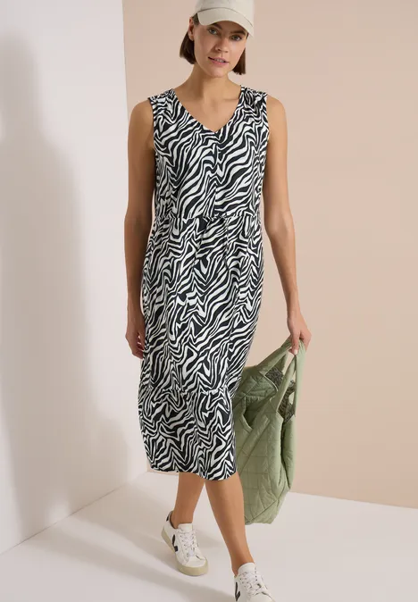 Frau in Zebra-Midikleid, weißer Sneaker, grüne Handtasche – lässiger, moderner Look.