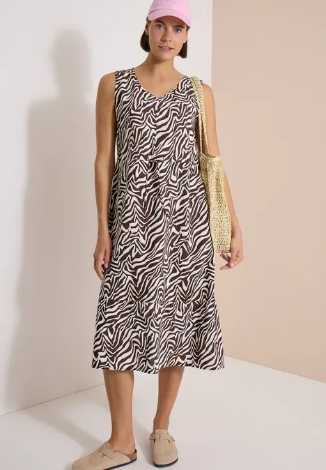 Femme porte une robe midi sans manches à motif zèbre et un sac jaune.