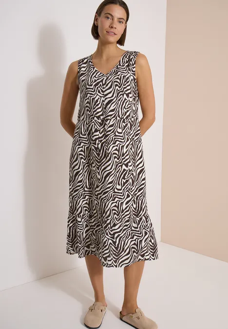 Femme en robe midi sans manches à motif zébré et mocassins beiges sur fond neutre.