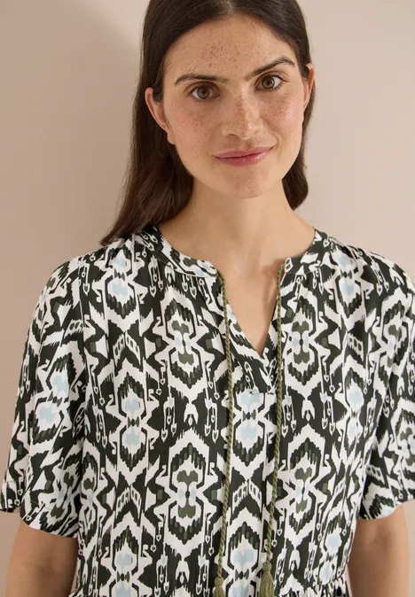 Eine Person trägt eine schwarz-weiße Bluse mit grafischem Muster.