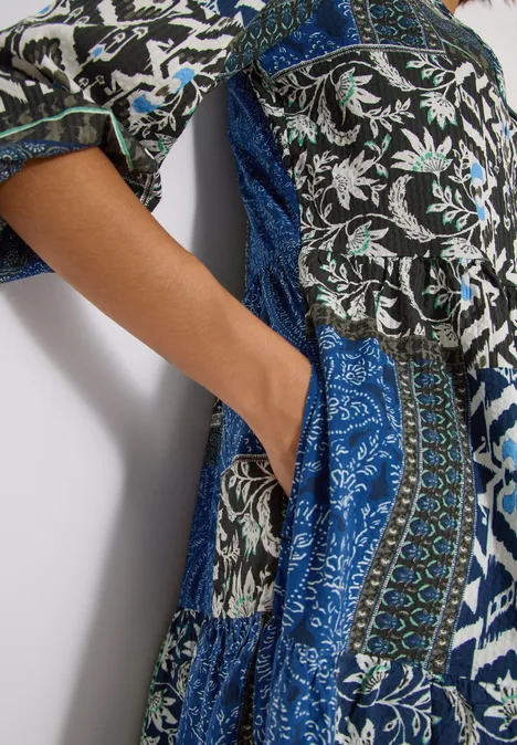 Hand in Seitentasche eines langen Kleides mit blauem, weißem und schwarzem Patchwork-Print.