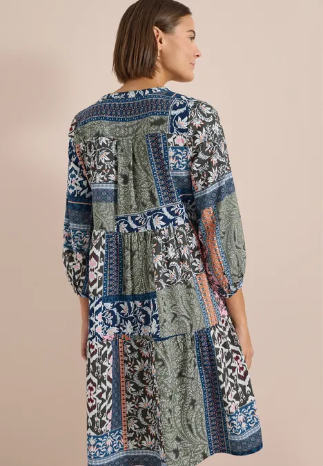 Frau von hinten in langem Patchworkkleid mit blau-grün-weißen Ornamentmustern.