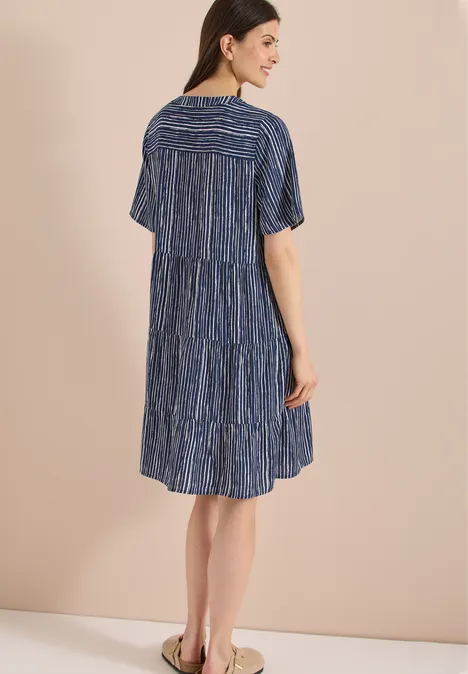 Frau von hinten in knielangem, kurzärmeligem, gestreiftem, stufigem, blauem Kleid.