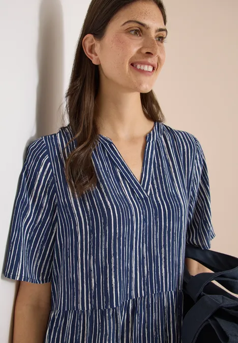 Frau trägt blau-weiß gestreiftes V-Ausschnitt-Kleid mit kurzen Ärmeln und leichter Taillennaht.