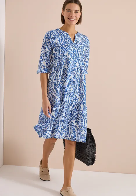 Dame in blau-weiß gemustertem Midikleid mit V-Ausschnitt, halblangen Ärmeln und Plattform-Sandalen.